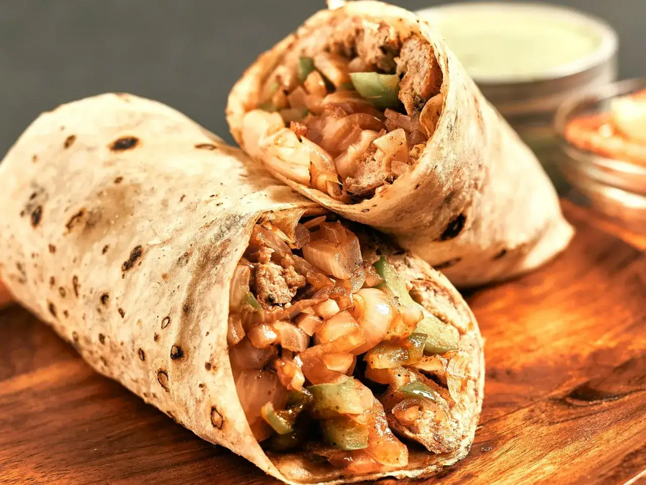 Dwa burritos z bogatym farszem z mięsa, cebuli i papryki na drewnianej desce.