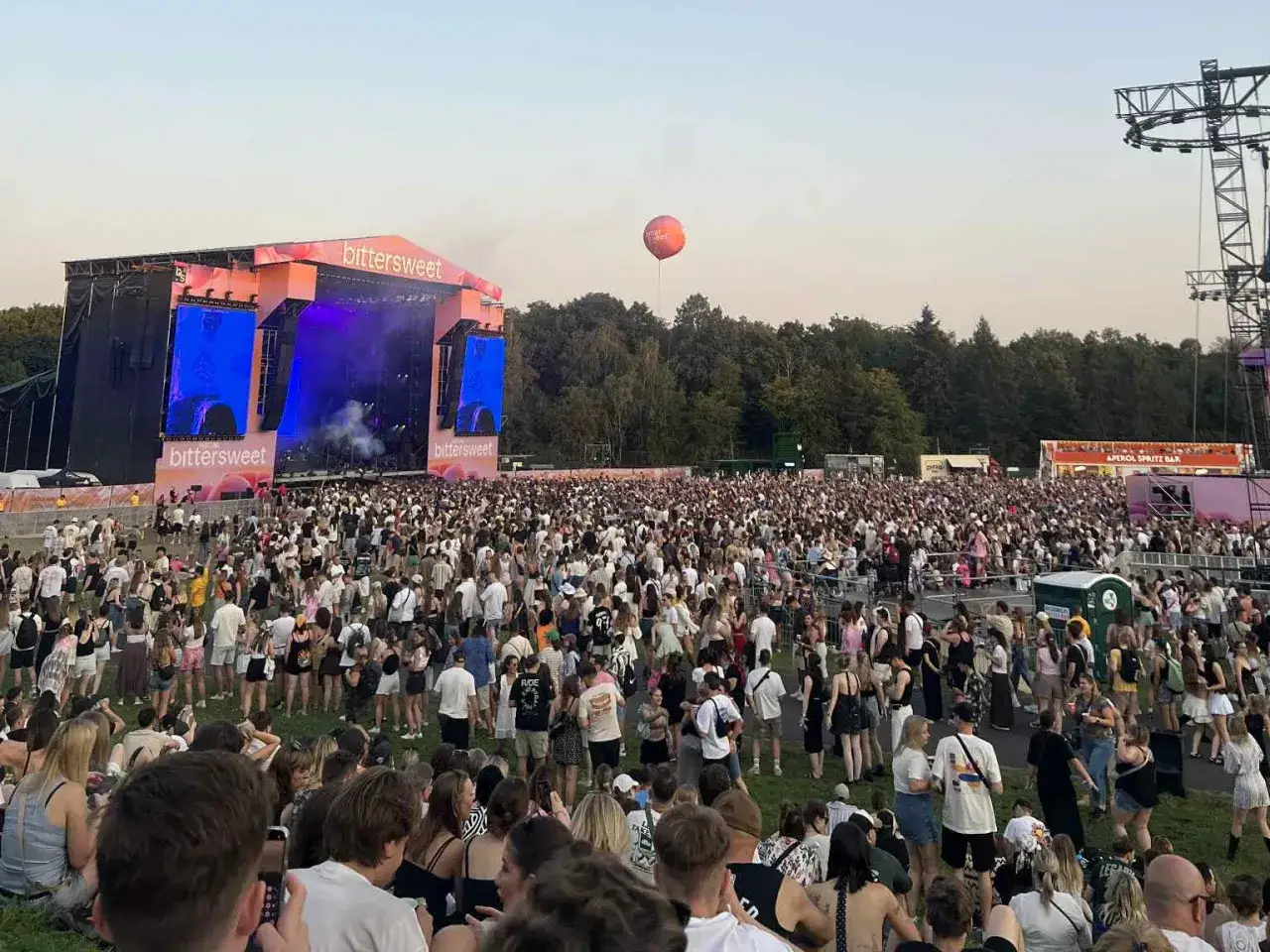 Tłum ludzi na festiwalu bittersweet, pod sceną z logo. W tle drzewa i niebo.