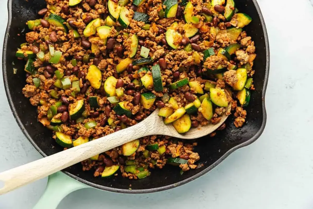 Herzhafte zucchini hackfleisch pfanne mit Bohnen und Paprika, serviert in einer Gusseisenpfanne mit einem Holzlöffel.