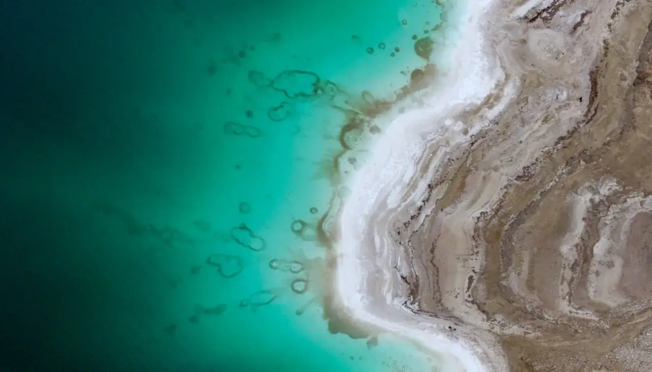 Luftaufnahme des Toten Meeres mit seinem extremen Salzgehalt, der sich in den einzigartigen Formationen am Ufer und im t&uuml;rkisfarbenen Wasser zeigt.