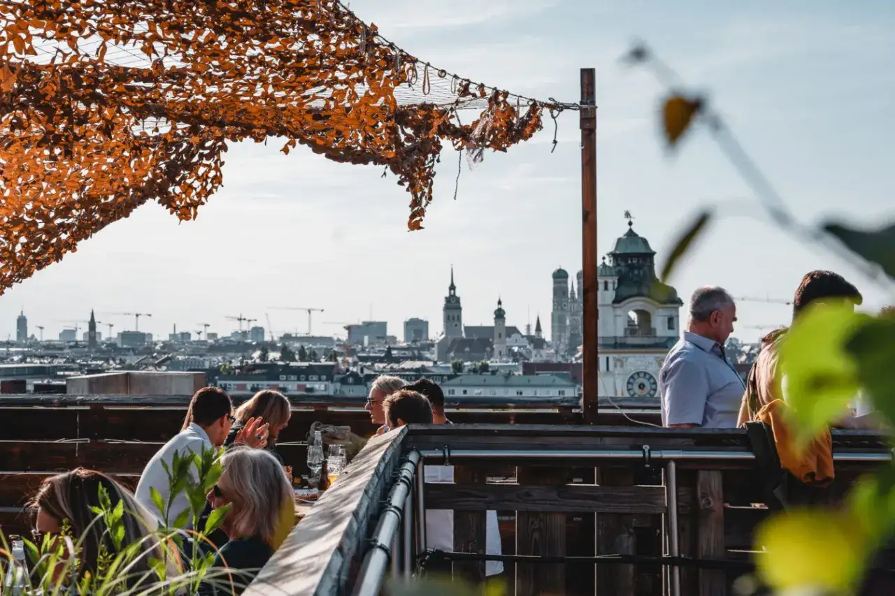 Menschen genie&szlig;en den Ausblick auf den **rooftop Munich** mit der Frauenkirche im Hintergrund.