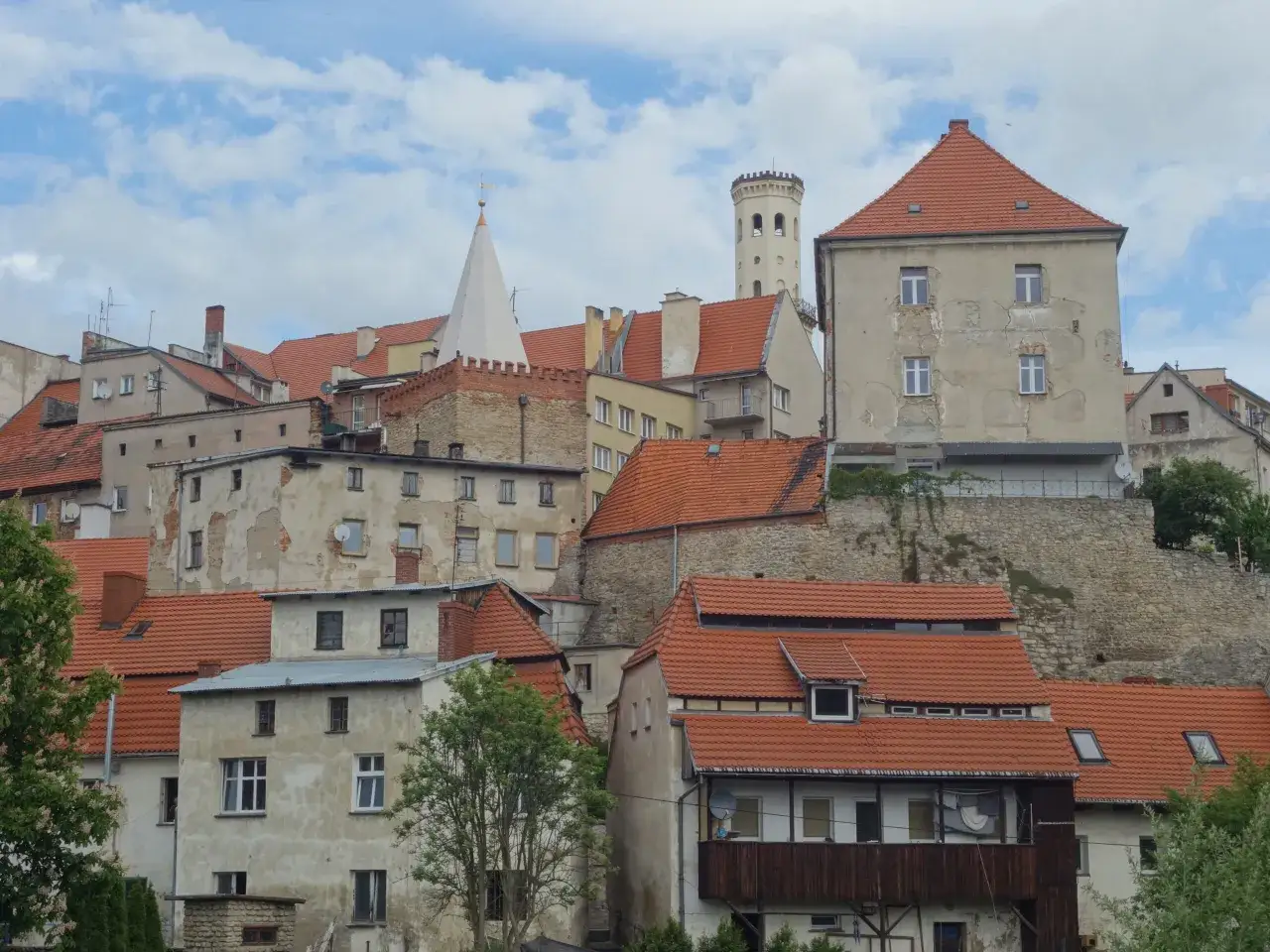 Widok na zabytkowe kamienice i wieżę w Bystrzycy Kłodzkiej. Dachy pokryte czerwona dachówką, niebo z chmurami.