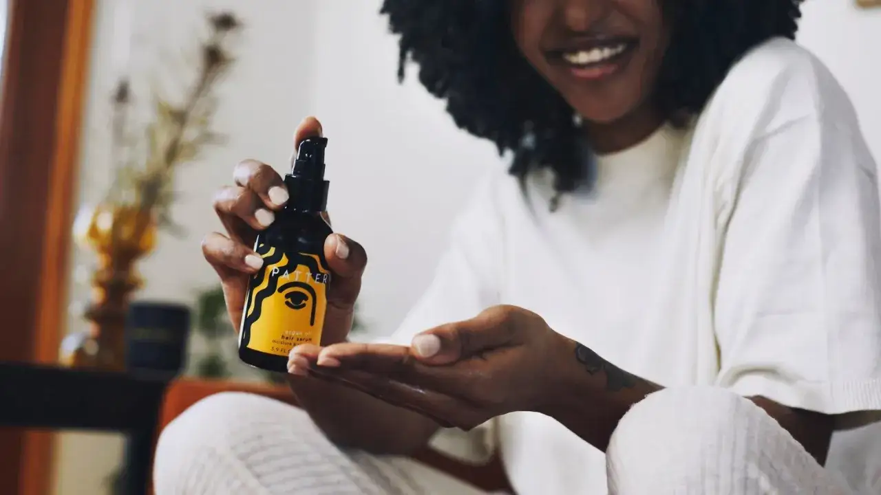 Donna sorridente applica oli naturali per capelli, un gesto di cura quotidiana per una chioma sana e luminosa.