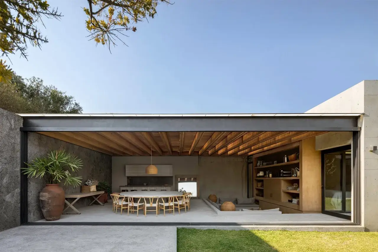 Un porche patio de casa moderno con mesa de comedor, cocina y &aacute;rea de estar integradas, abierto al exterior.
