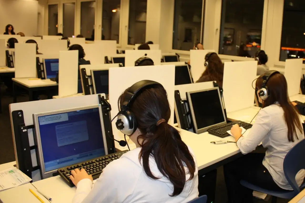 Estudiantes con auriculares realizan un examen en un aula de **computer based Cambridge**.