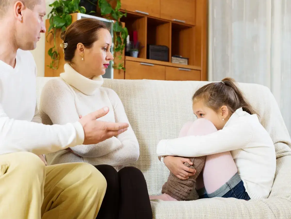 Padres discuten mientras su hija se acurruca, sintiendo que deben decir no a los ni&ntilde;os.
