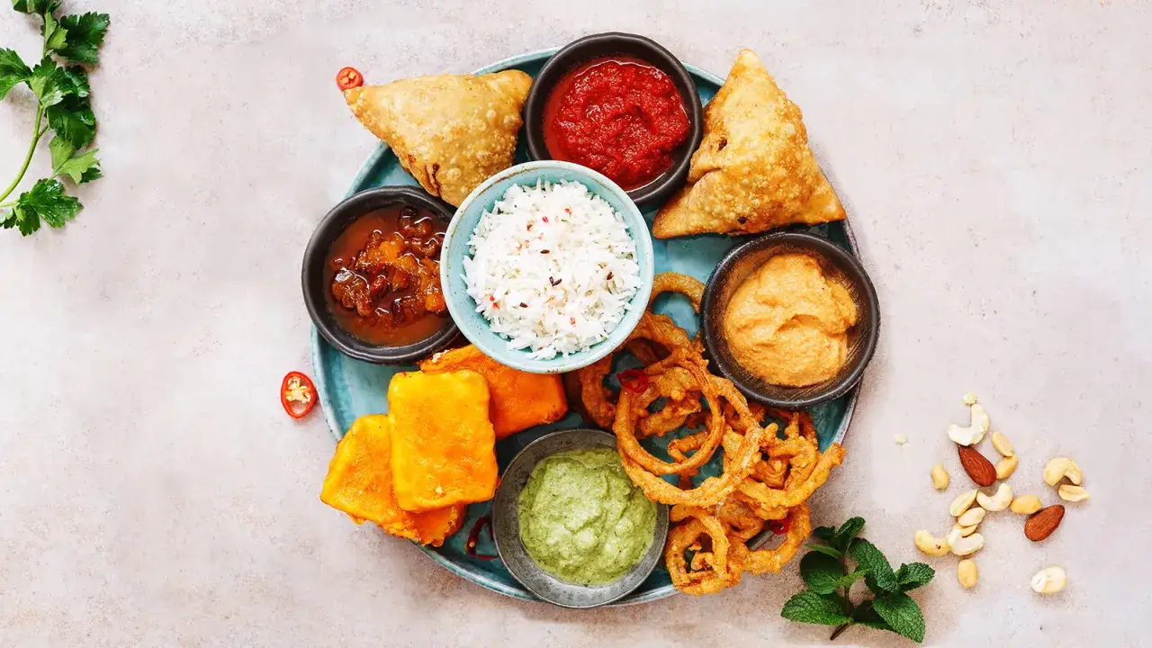 En bricka med indisk mat: samosas, ris, pakora, l&ouml;kringar och olika indisk s&aring;s.
