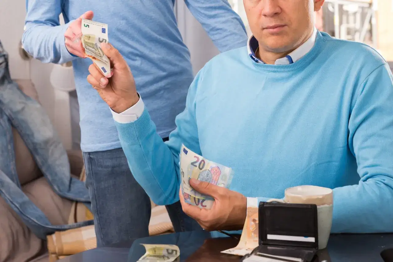 Un figlio che ruba soldi ai genitori, con banconote da 5 e 20 euro in mano.