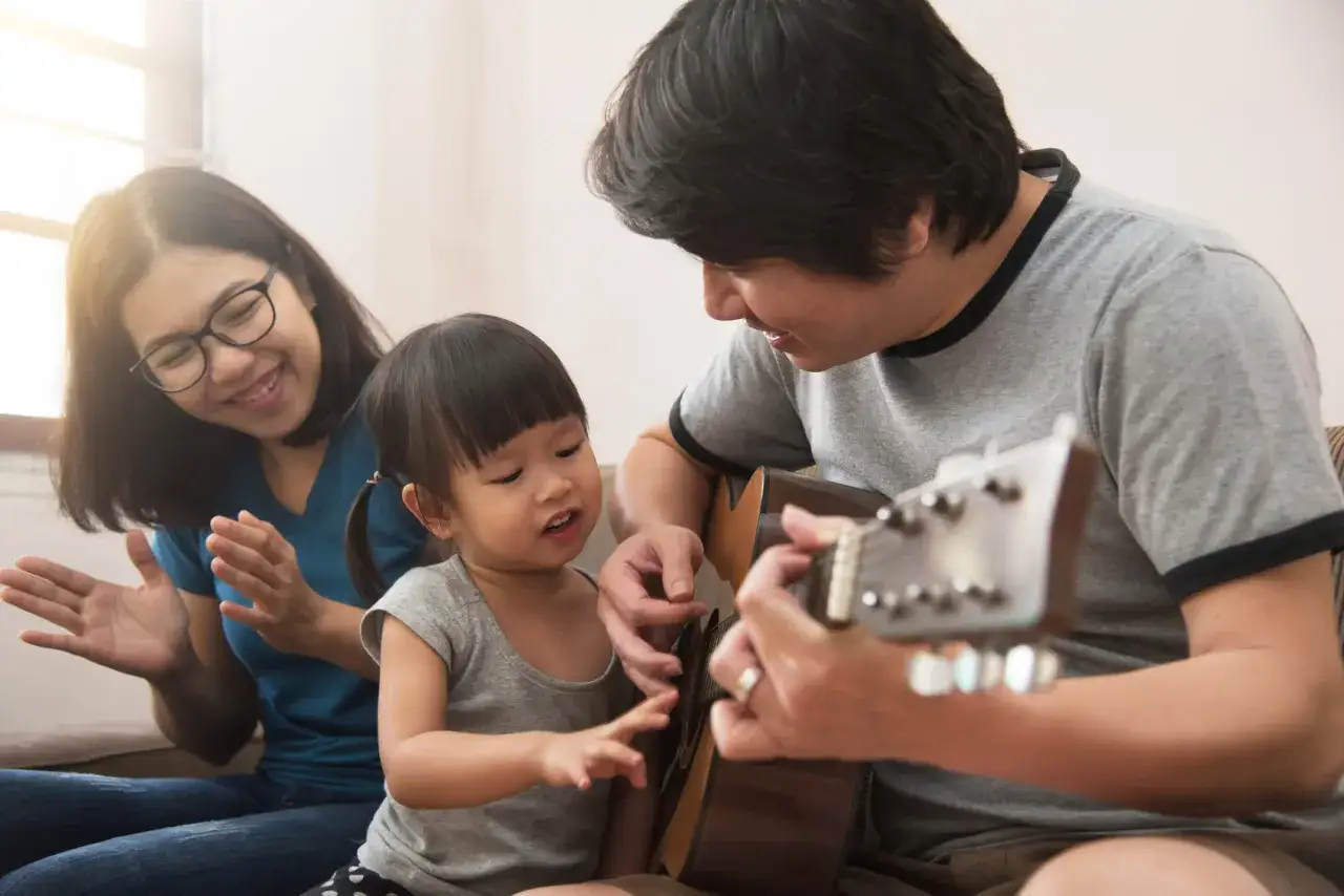 Famiglia felice che suona la chitarra, creando canzoni dedicate ai figli. La mamma batte le mani, il pap&agrave; insegna alla bimba.