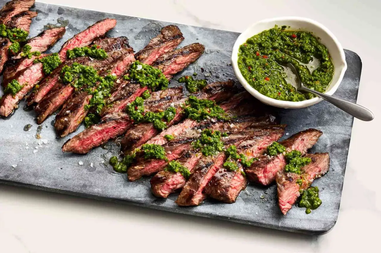 Grillad entra&ntilde;a de res, skivad och toppad med gr&ouml;n chimichurris&aring;s, serverad p&aring; en stenplatta.