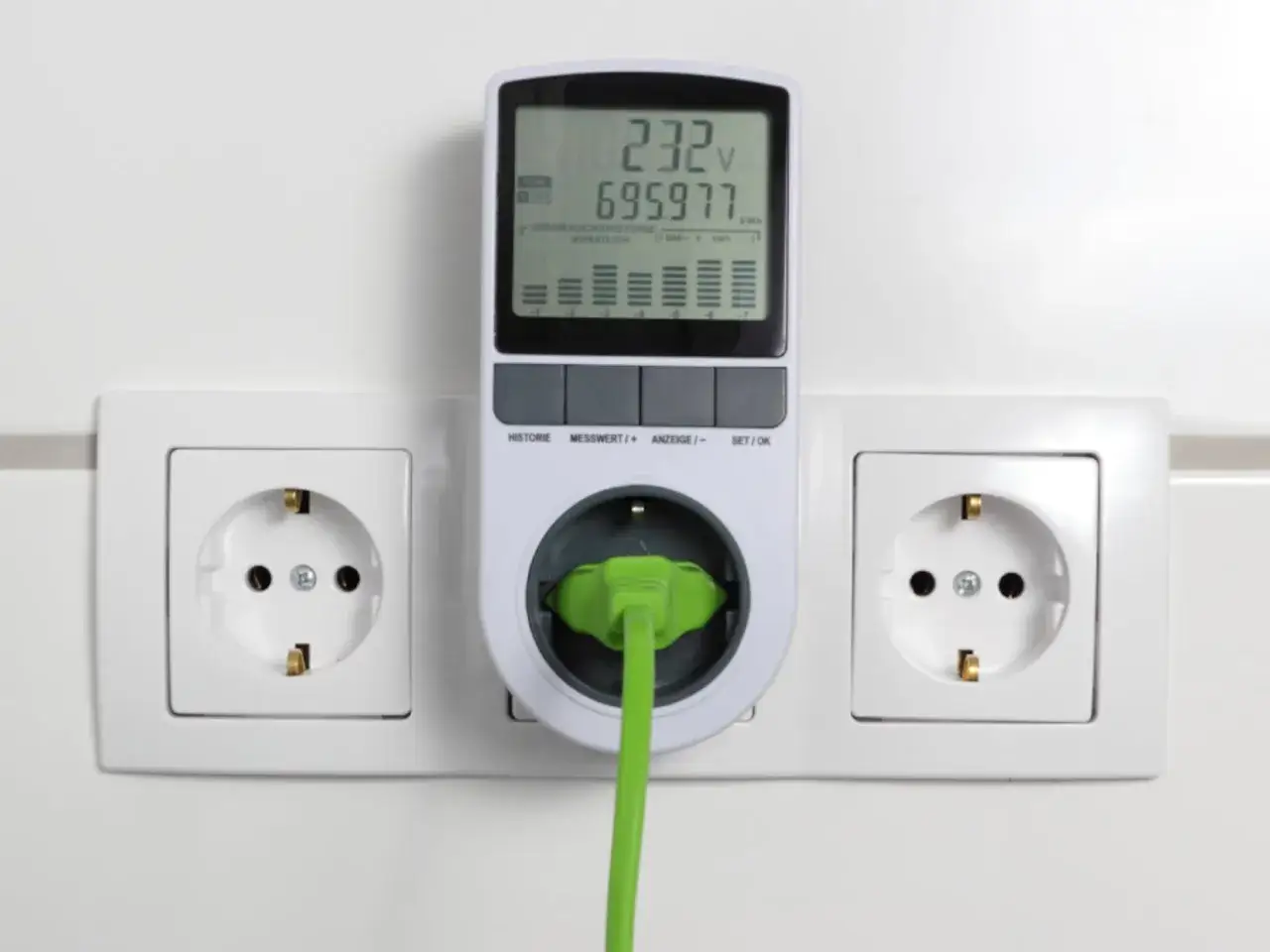 Medidor de consumo eléctrico enchufado a una toma de corriente. Muestra voltaje y kWh, ayudando a entender como se mide el consumo electrico.