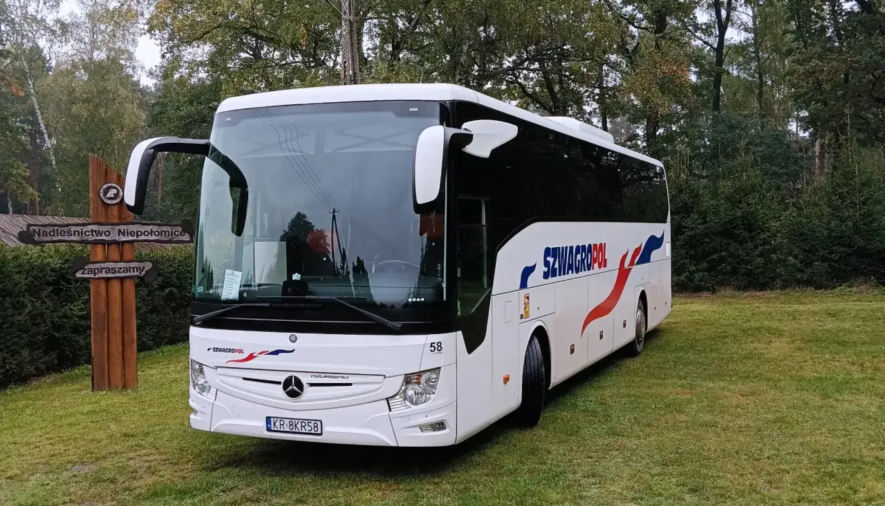 Biały autokar Szwagropol na trawie, obok drewniany drogowskaz 