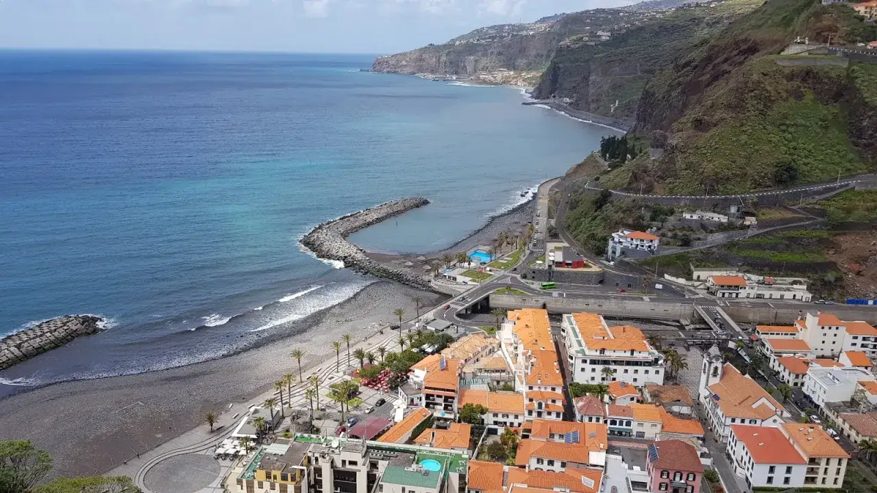 Blick auf Ribeira Brava mit seinem steinigen Strand, dem Hafen und den weißen Häusern mit roten Ziegeldächern, die sich an die steilen Hänge schmiegen.