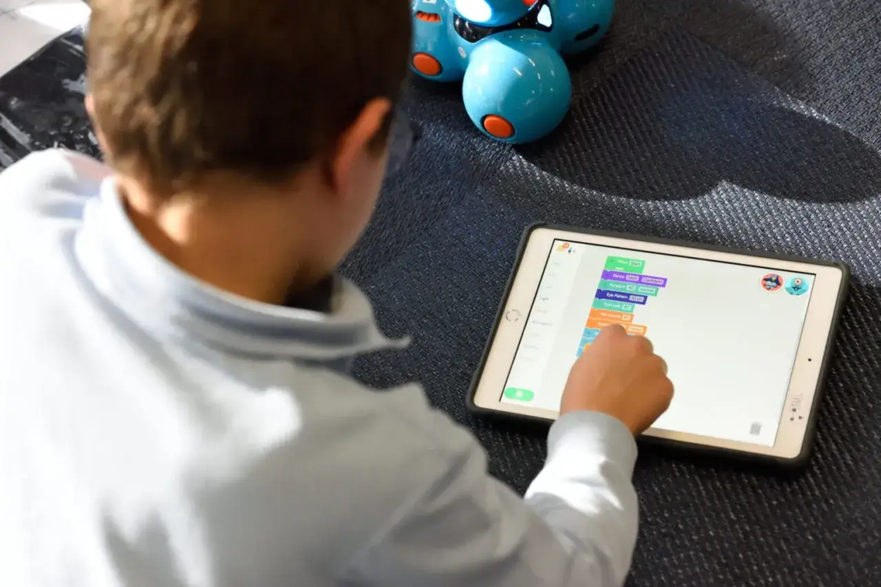 Chłopiec programuje robota na tablecie, tworząc sekwencję poleceń. Qustodio pomaga rodzicom nadzorować aktywność dzieci w internecie.
