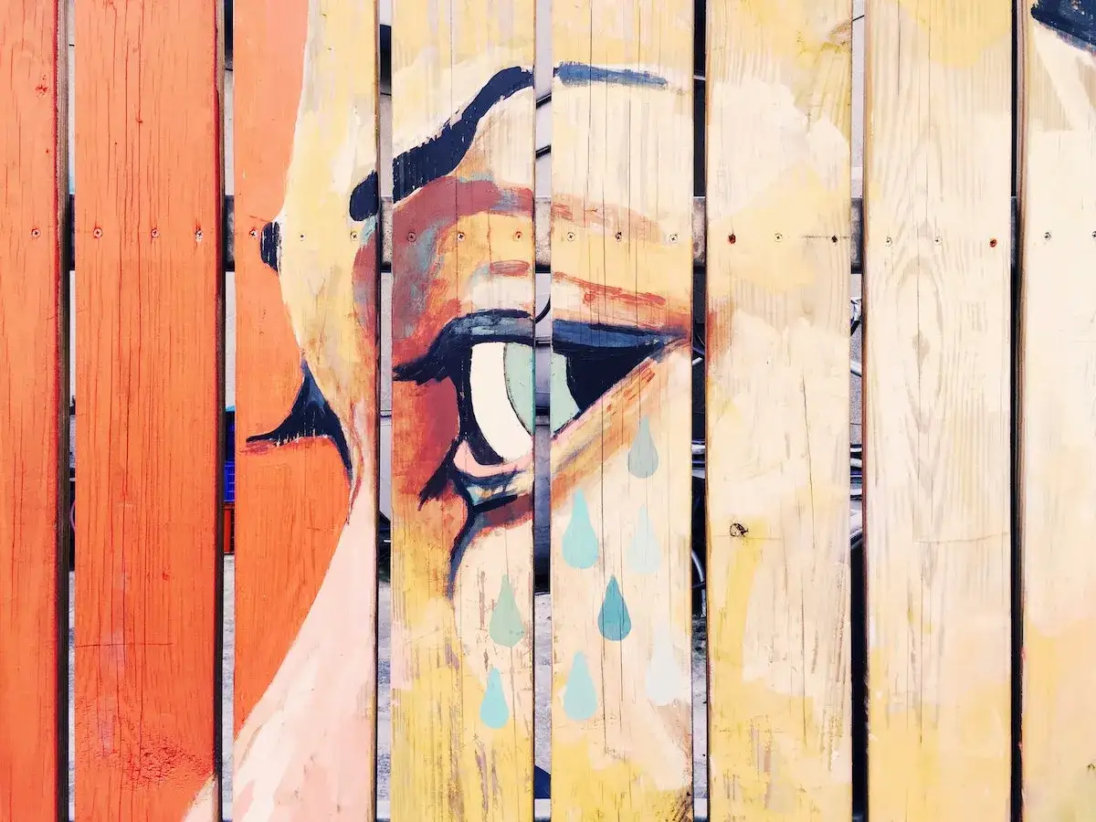 Œuvre d'un artiste peintre sur bois : un œil expressif aux larmes bleues sur une clôture en planches.