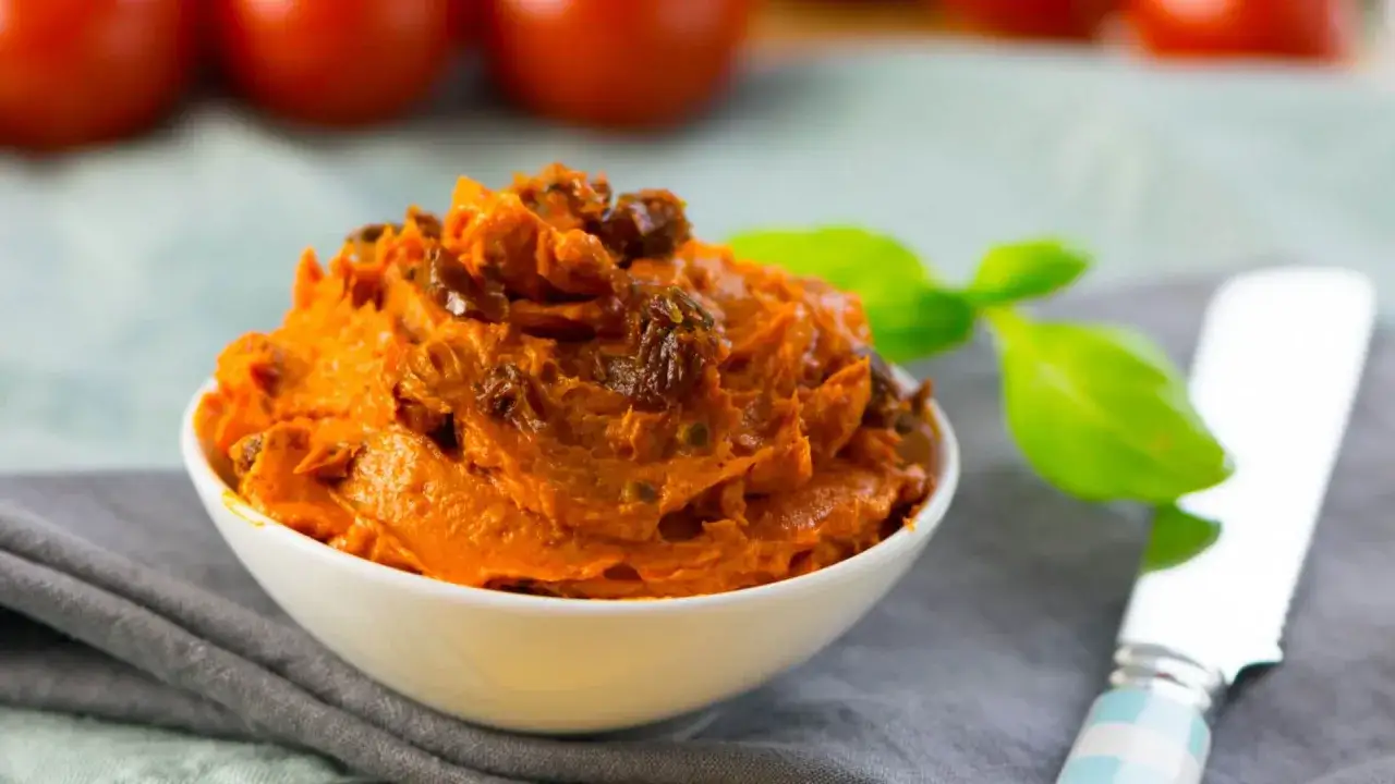 Cremige italienische Tomatenbutter mit getrockneten Tomatenstückchen in einer Schale, garniert mit Basilikum.