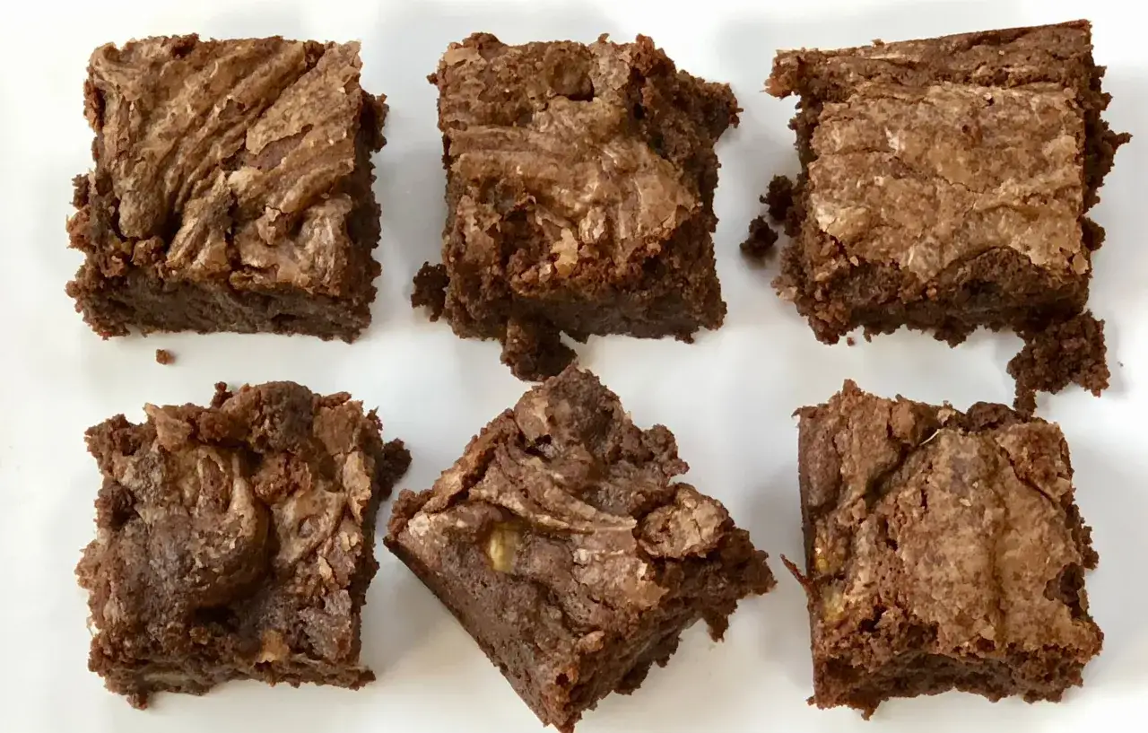 Sechs saftige Bananen-Brownies mit marmorierter Oberfl&auml;che auf wei&szlig;em Teller.