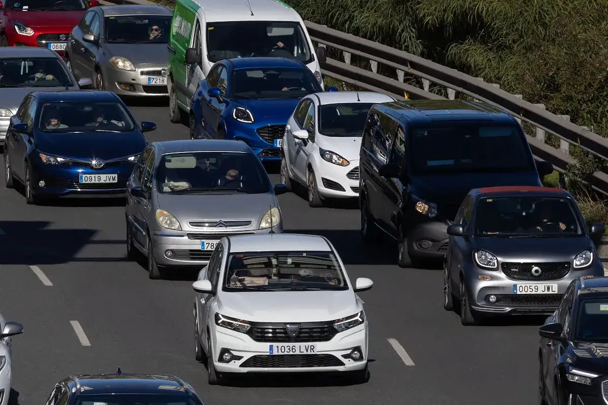 Tr&aacute;fico denso en una autopista, con muchos coches y furgonetas, contribuyendo a la **contaminaci&oacute;n de coches**.