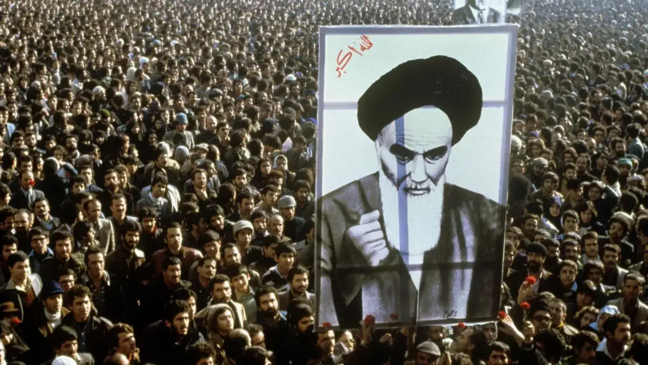 Massen versammeln sich bei der islamischen Revolution 1979 im Iran, ein gro&szlig;es Portr&auml;t von Ayatollah Khomeini wird hochgehalten.