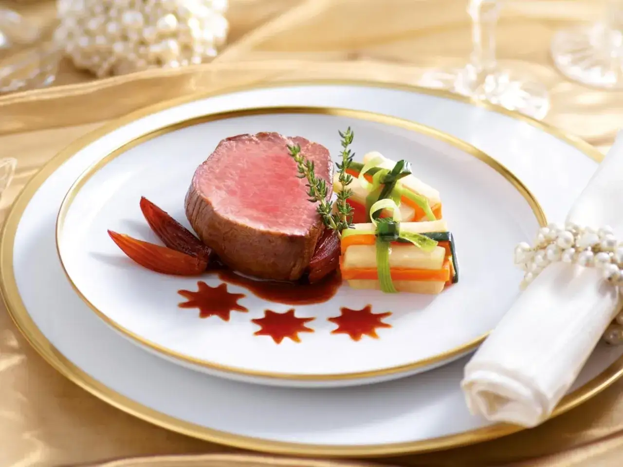 Zartes Rinderfilet mit Portweinsauce, garniert mit Gemüse und Kräutern, auf einem eleganten Teller mit goldenem Rand.