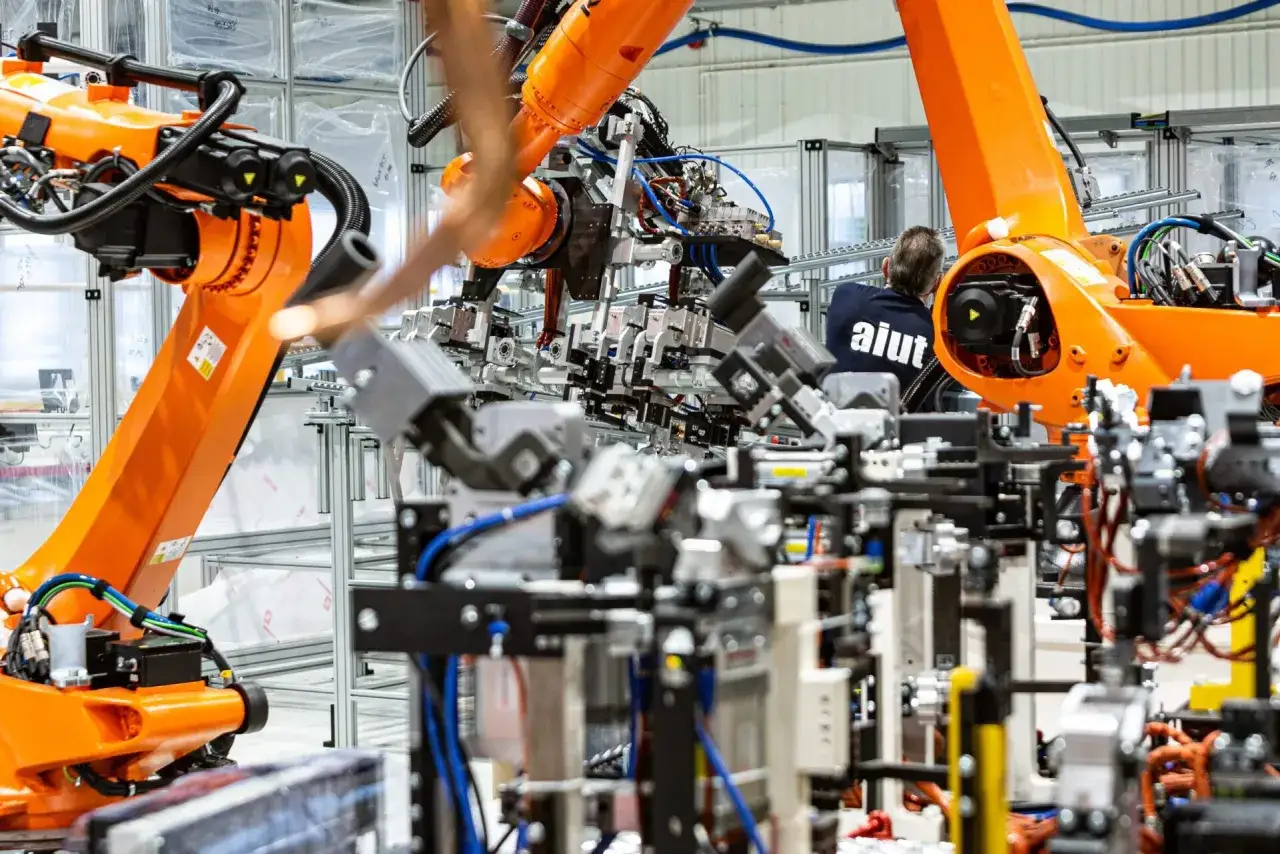 Pomarańczowe ramiona robot&oacute;w pracują w fabryce, gdzie system MES zarządza produkcją.