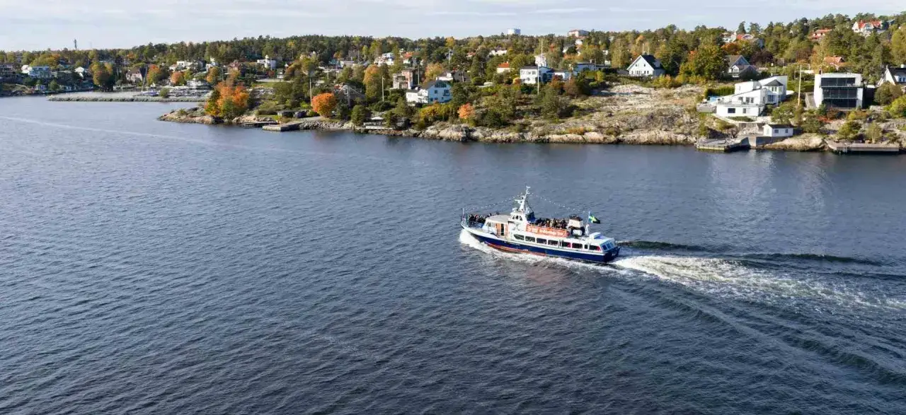 En båt med passagerare gör båtutflykter i Stockholm, med vackra hus och träd längs stranden.