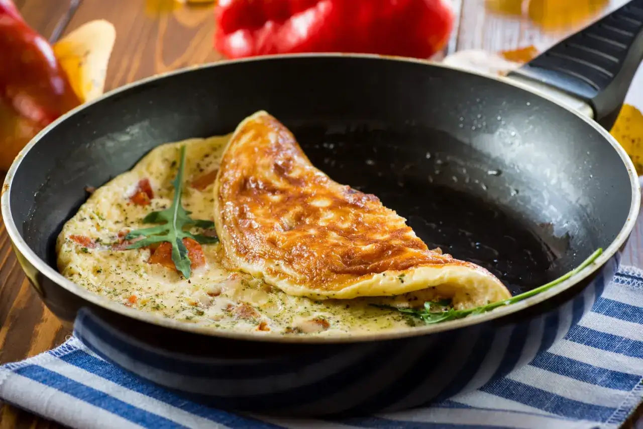 Une omelette dor&eacute;e et moelleuse, garnie de tomates et d'herbes, cuite dans une po&ecirc;le.
