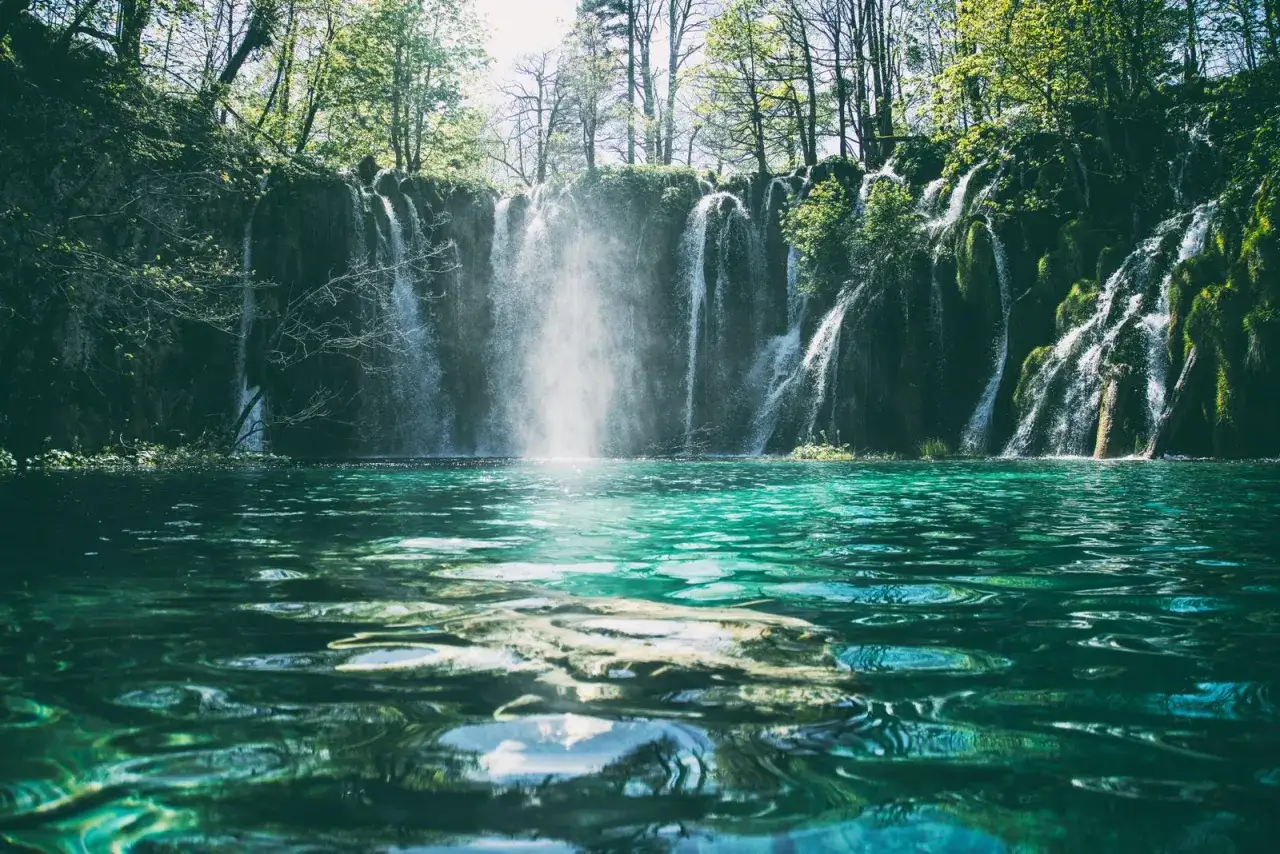 Un exuberante camino del agua con cascadas cayendo sobre rocas cubiertas de musgo en un lago turquesa.