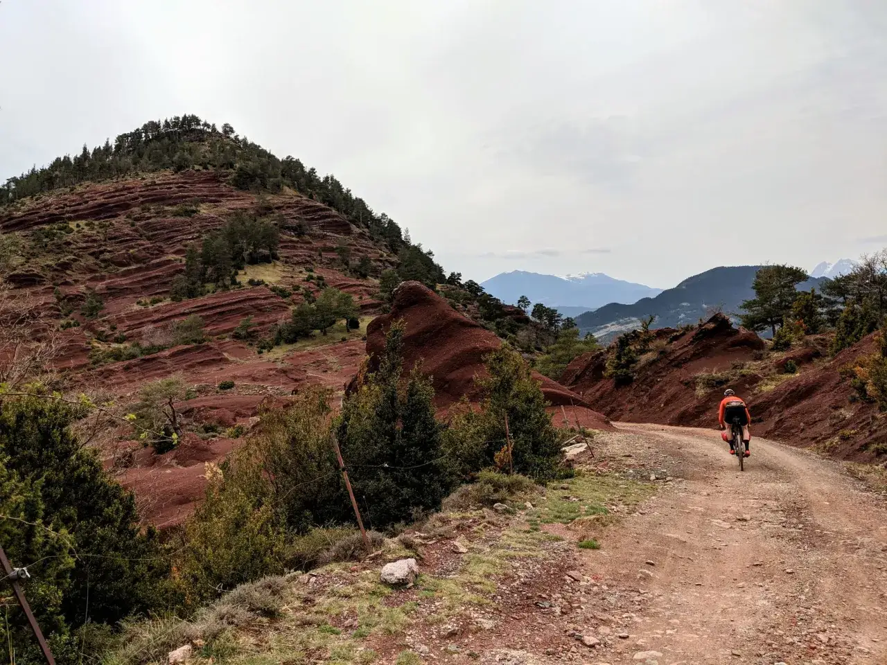 Ciclista en un camino de tierra rojiza, explorando las impresionantes **rutas en bici Catalunya**. Paisaje montañoso con formaciones rocosas únicas.