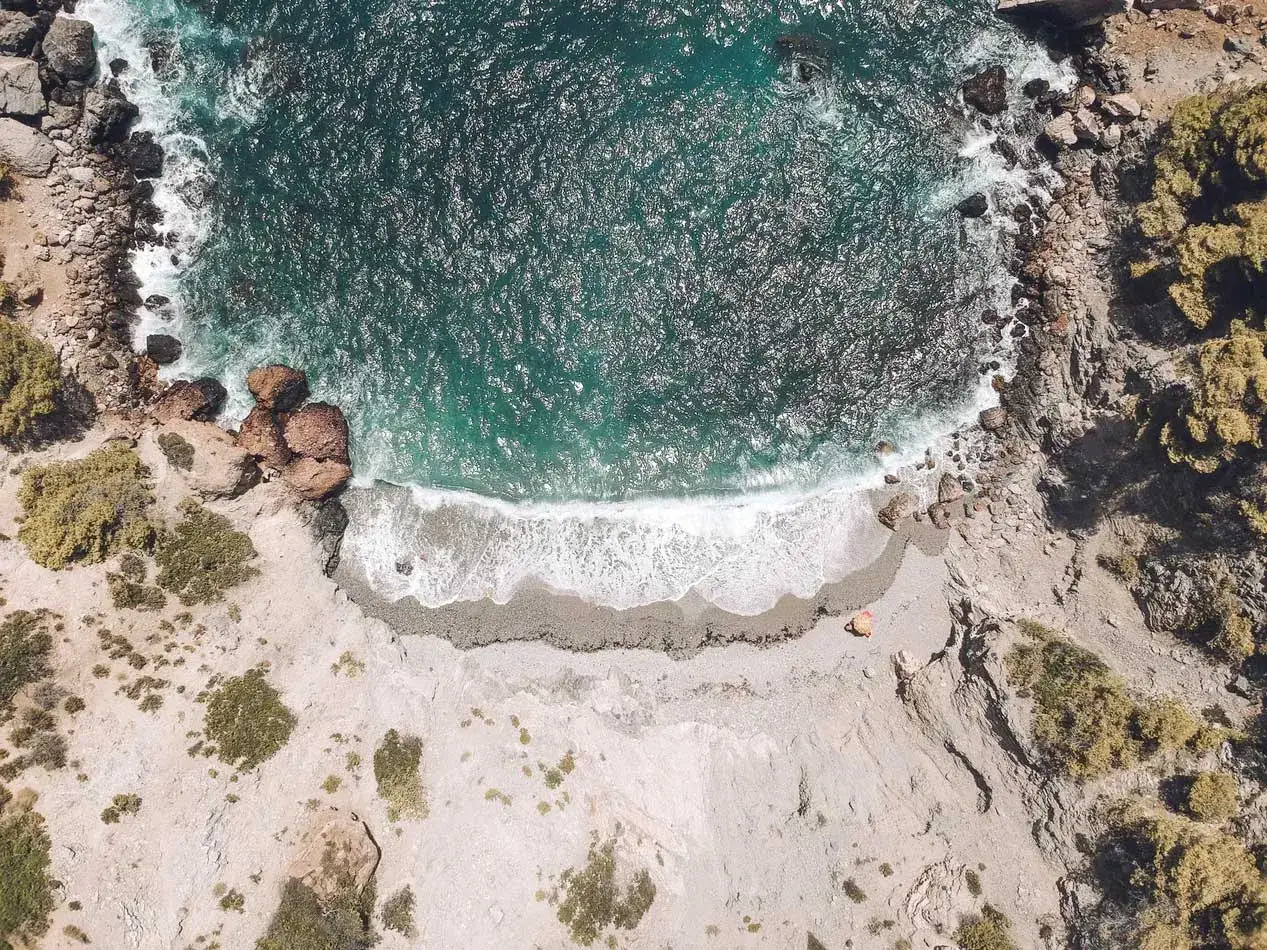 Vista aérea de una cala rocosa con aguas turquesas, una pequeña playa de guijarros y vegetación. Un paraíso entre las mejores playas del Levante.