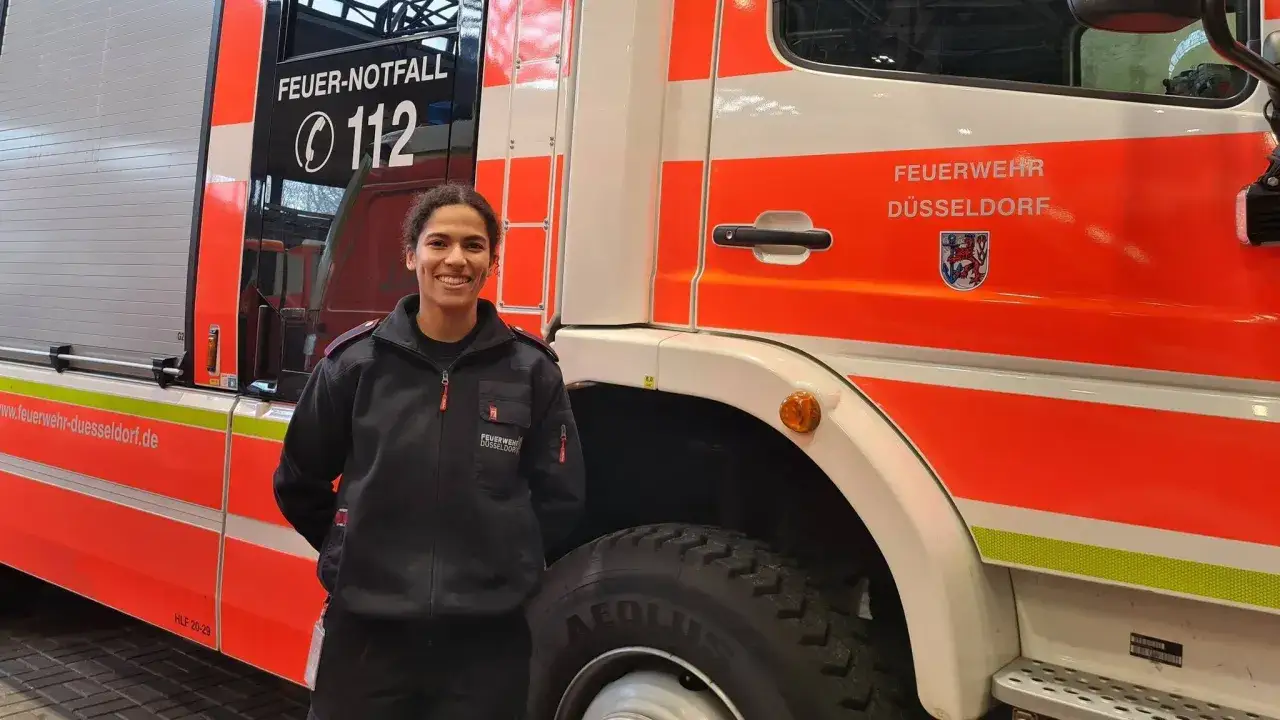 Eine junge Frau in Uniform steht vor einem Feuerwehrauto in D&uuml;sseldorf. Sie l&auml;chelt und wirkt stolz. So wird man Feuerwehrfrau!