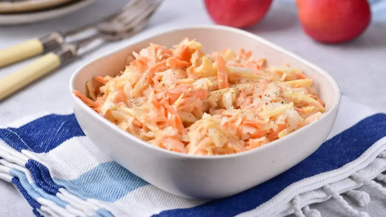 Sałatka coleslaw z marchewką i jabłkiem, doprawiona pieprzem. Kolor pomarańczy jest intensywny.