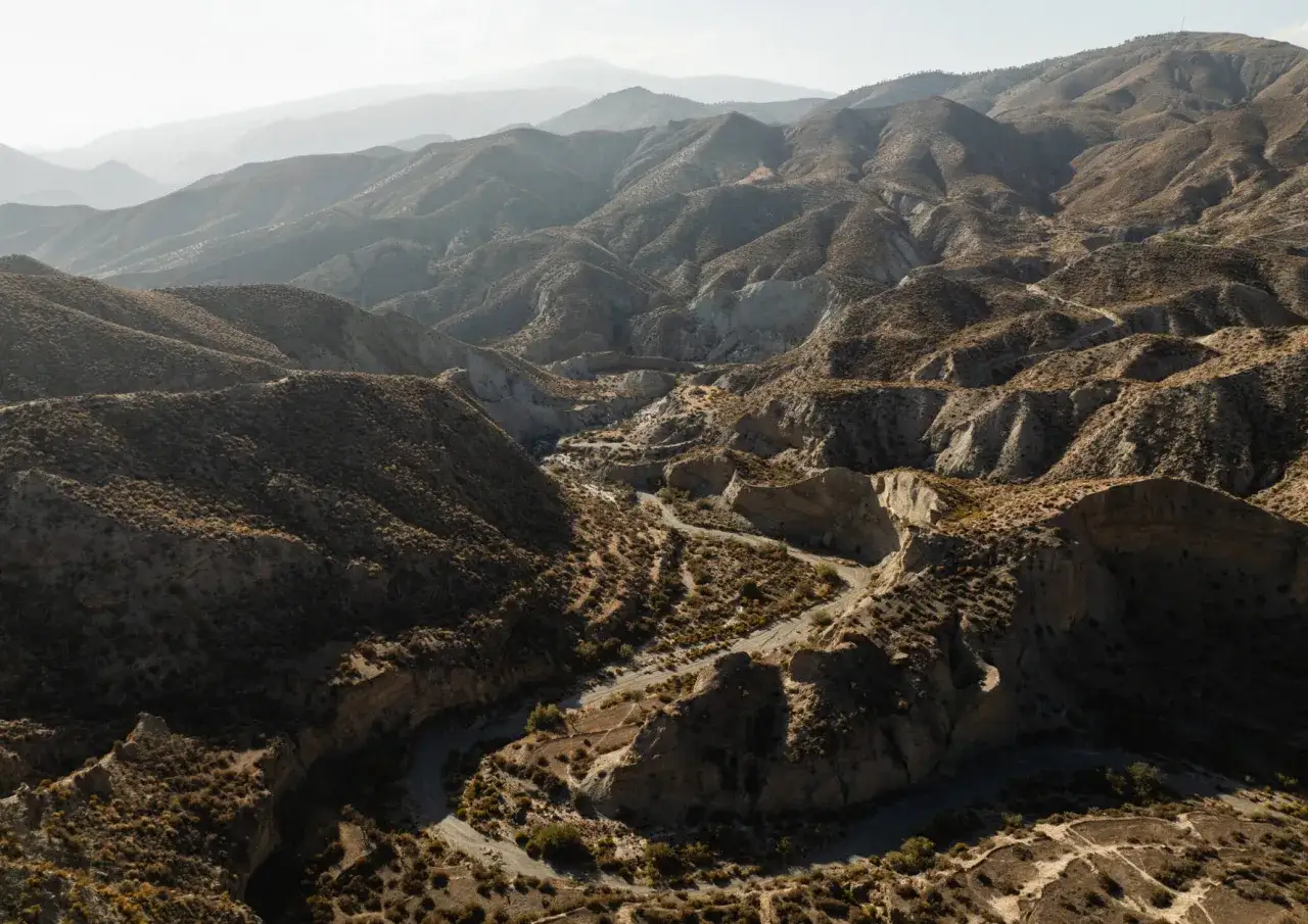 Paisaje árido y montañoso, ideal para visitar el Desierto de Tabernas. Carreteras serpenteantes atraviesan barrancos y colinas cubiertas de vegetación escasa.