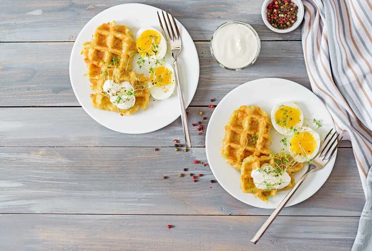 Due piatti con waffle salati, uova sode e yogurt greco, un'idea per una colazione senza scorie.