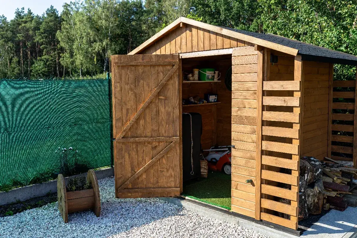 Abri de jardin en bois ouvert, montrant des outils et une tondeuse. La question