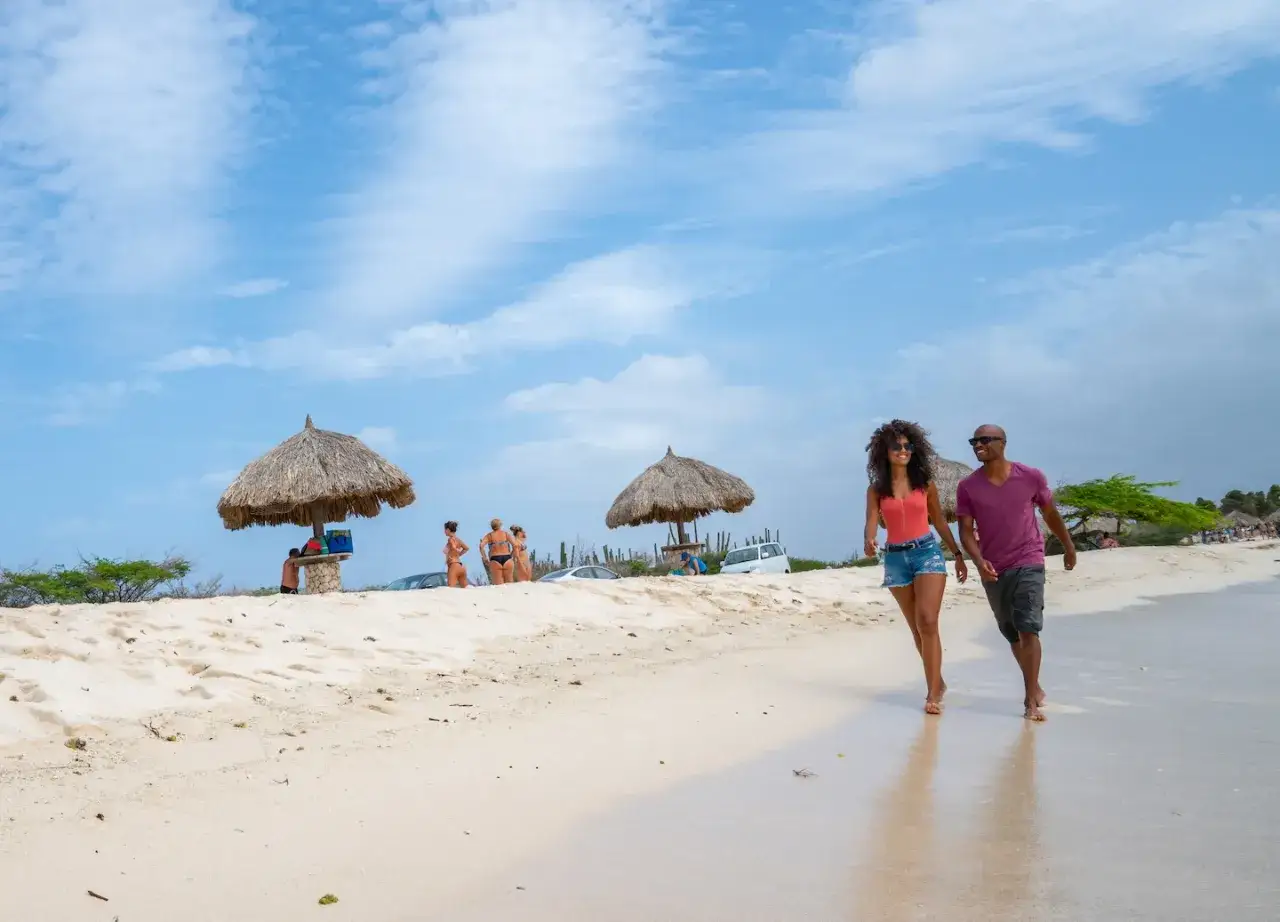 Ett par promenerar p&aring; stranden p&aring; Aruba i december. V&auml;dret &auml;r soligt med moln p&aring; himlen.