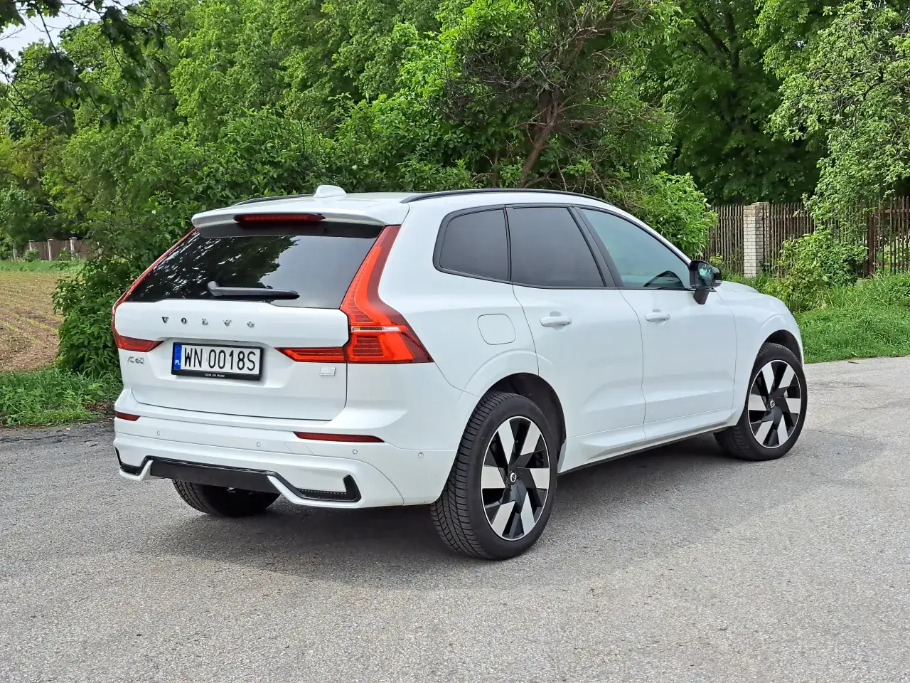Białe Volvo XC60 na tle zieleni. Zastanawiasz się, ile spala Volvo XC60? Ten SUV oferuje komfort i bezpieczeństwo.