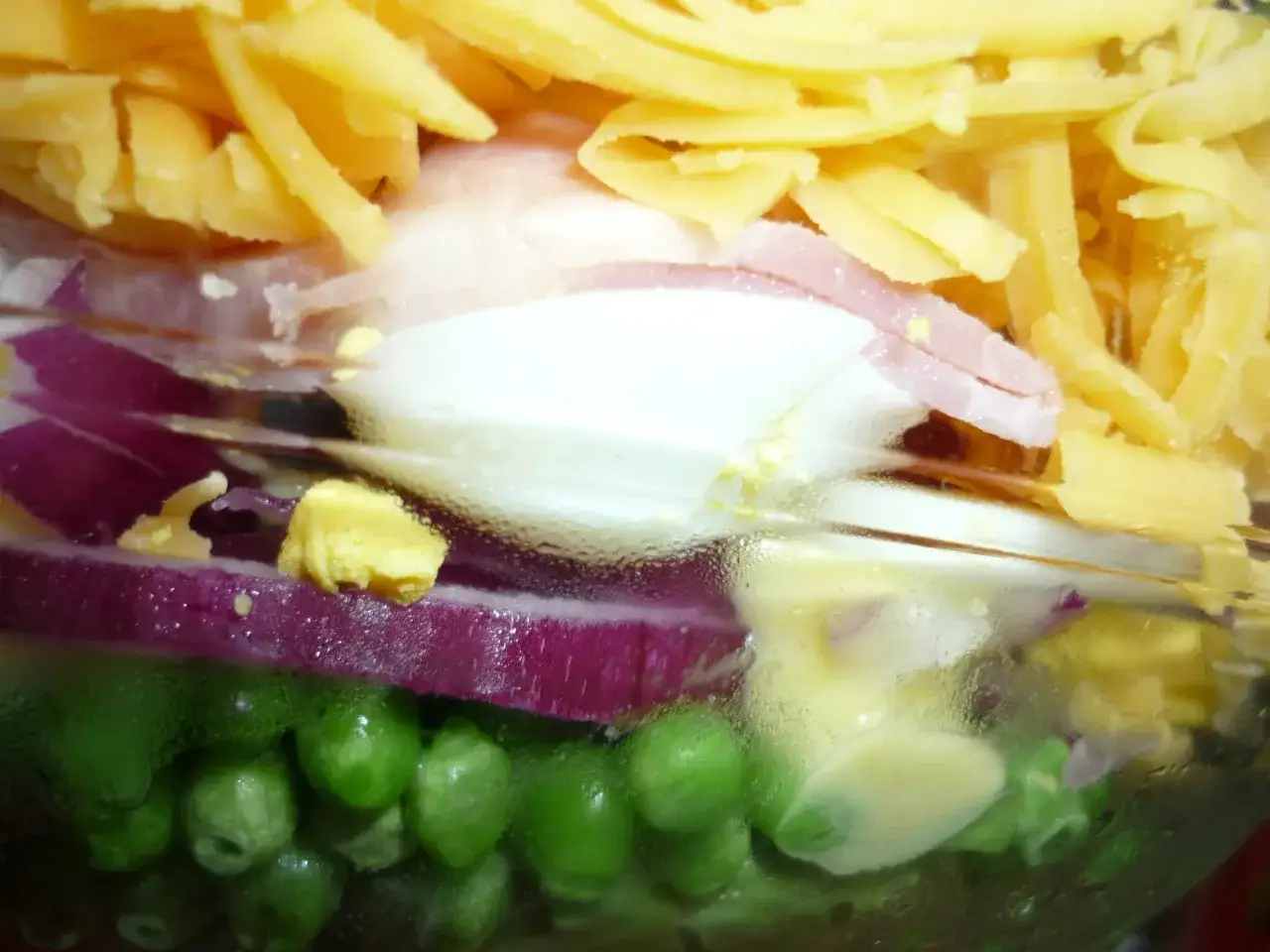 Une salade 7 &eacute;tages color&eacute;e dans un bocal : petits pois, oignons rouges, &oelig;ufs, jambon et fromage r&acirc;p&eacute;.