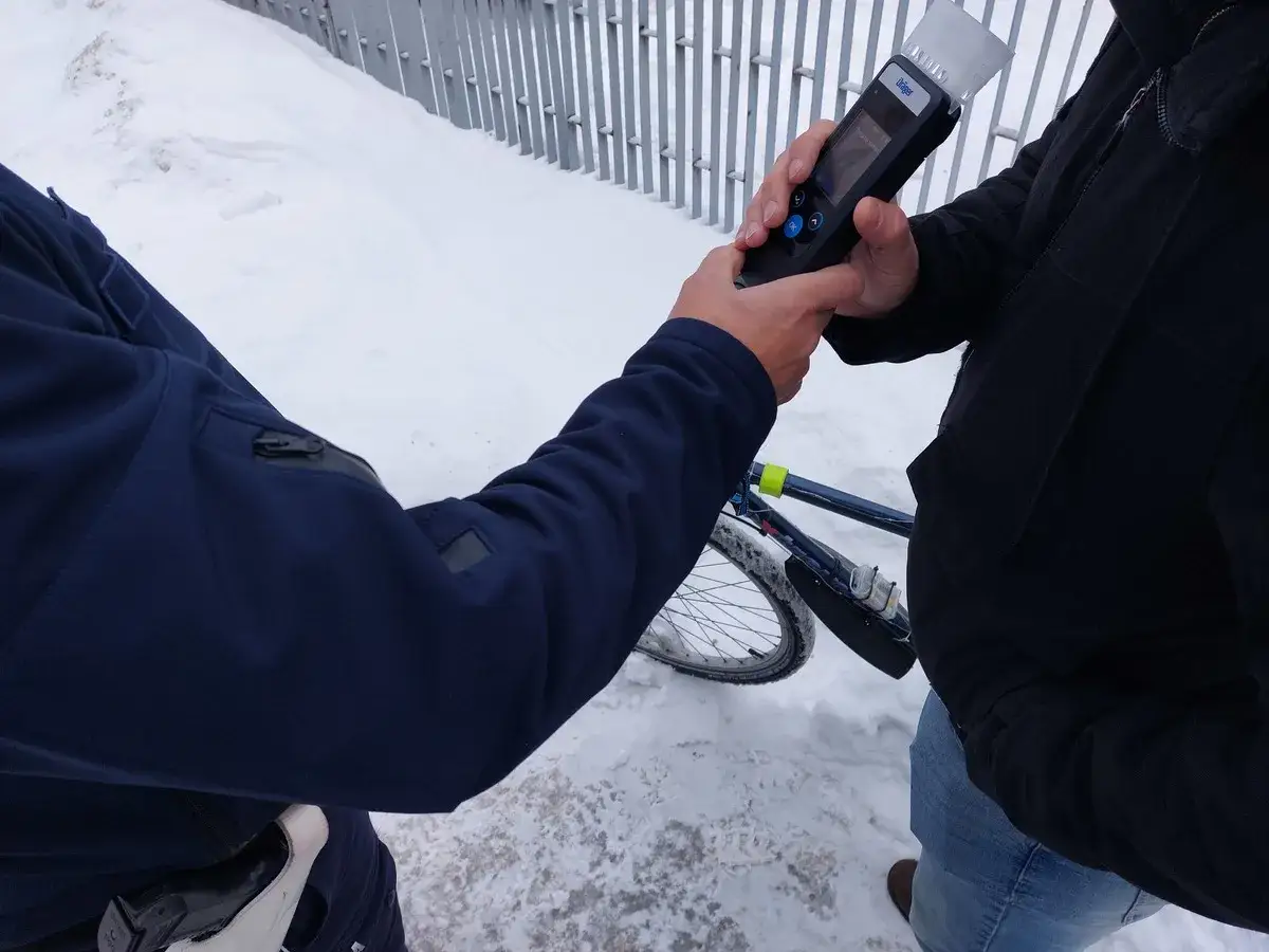 Policjant bada alkomatem rowerzystę. Niebezpieczna jazda rowerem po alkoholu może skończyć się kontrolą.