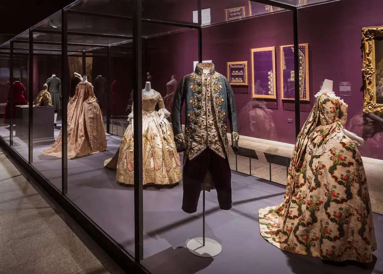 Prunkvolle Kleider und ein bestickter Herrenrock erzählen die Geschichte der Mode in einer Museumsausstellung.