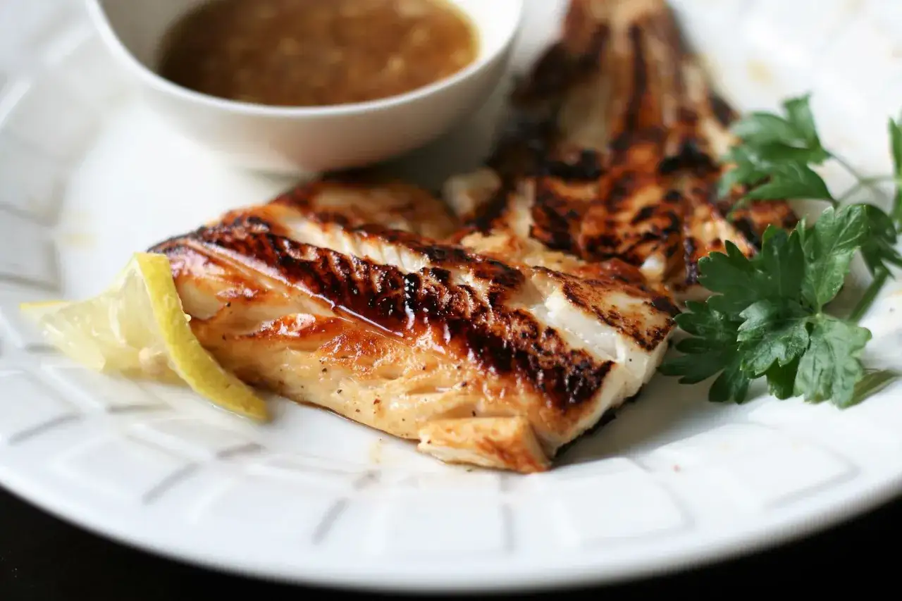 Grillowany halibut ryba z cytryną i natką pietruszki, podany z sosem.