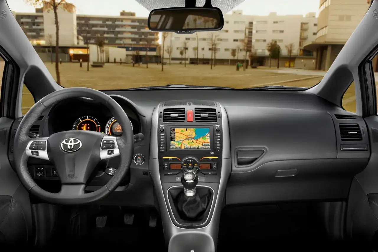 Wnętrze Toyoty Auris 2010 z widocznym kokpitem, kierownicą i ekranem nawigacji.
