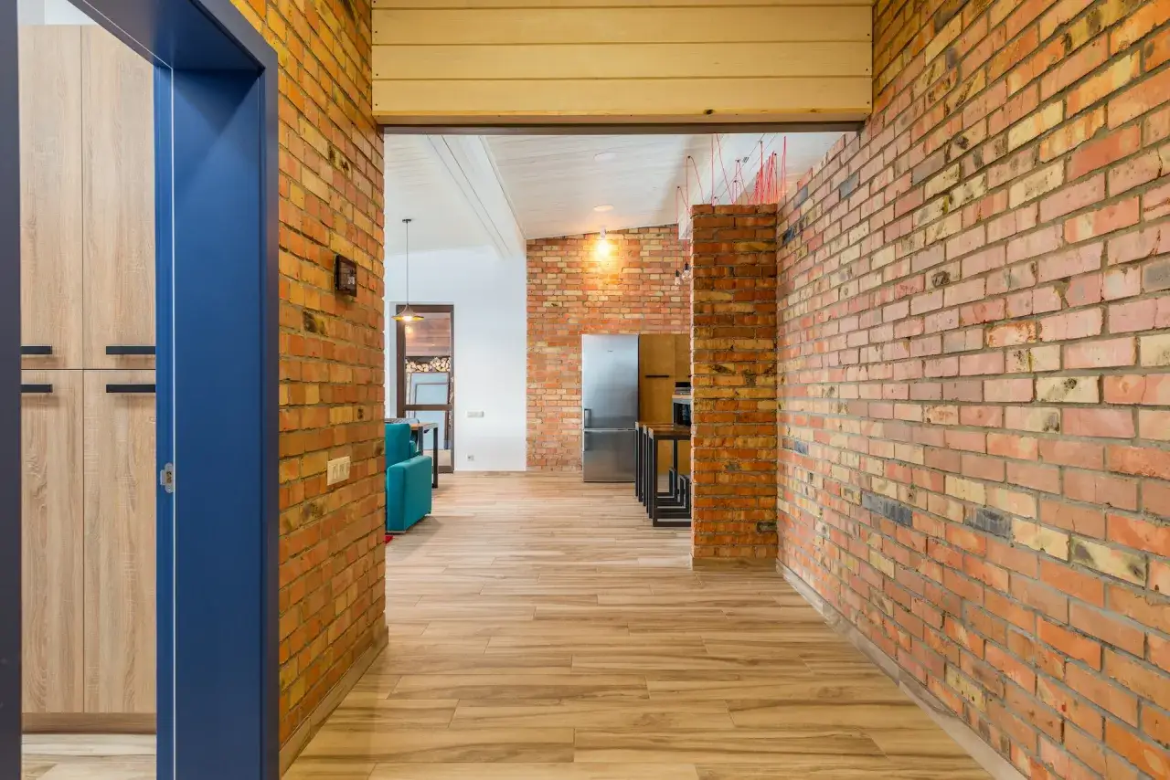 Przedpok&oacute;j loft inspiracje: ceglane ściany, drewniana podłoga i niebieskie drzwi tworzą industrialny klimat.