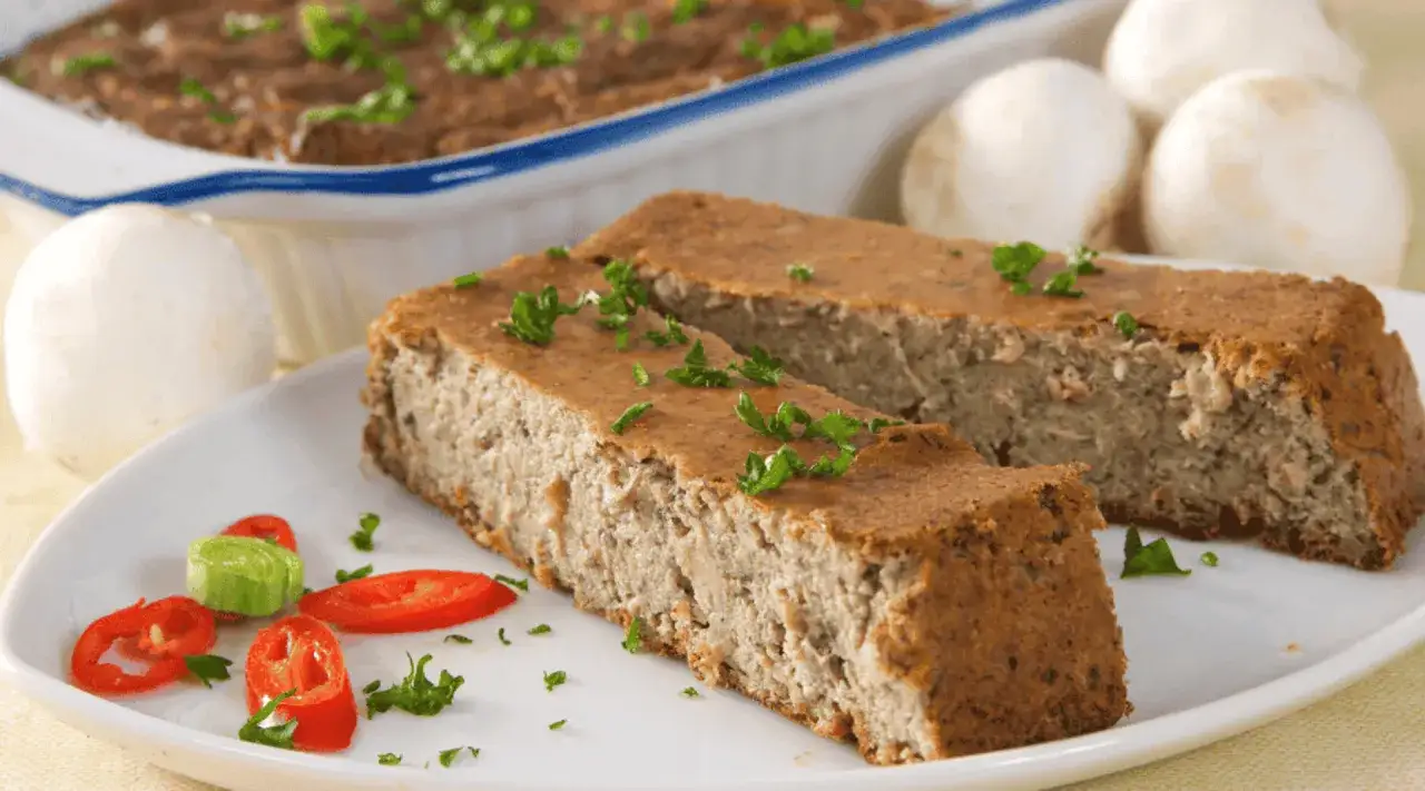 Dwa kawałki domowego pasztetu z królika, ozdobione natką pietruszki, na talerzu z plasterkami papryczki chili i ogórka.