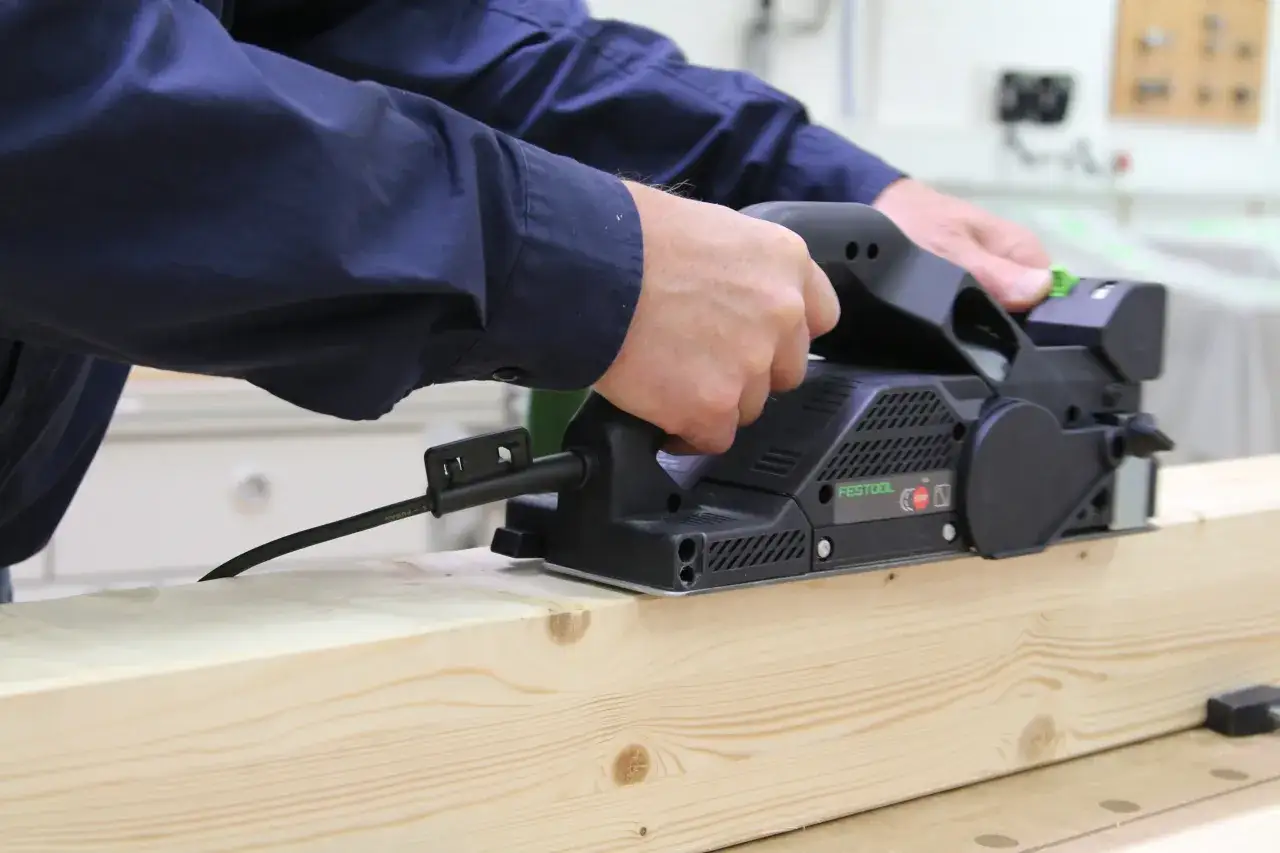 Mains raboteuse Festool en action, lissant une planche de bois avec pr&eacute;cision.