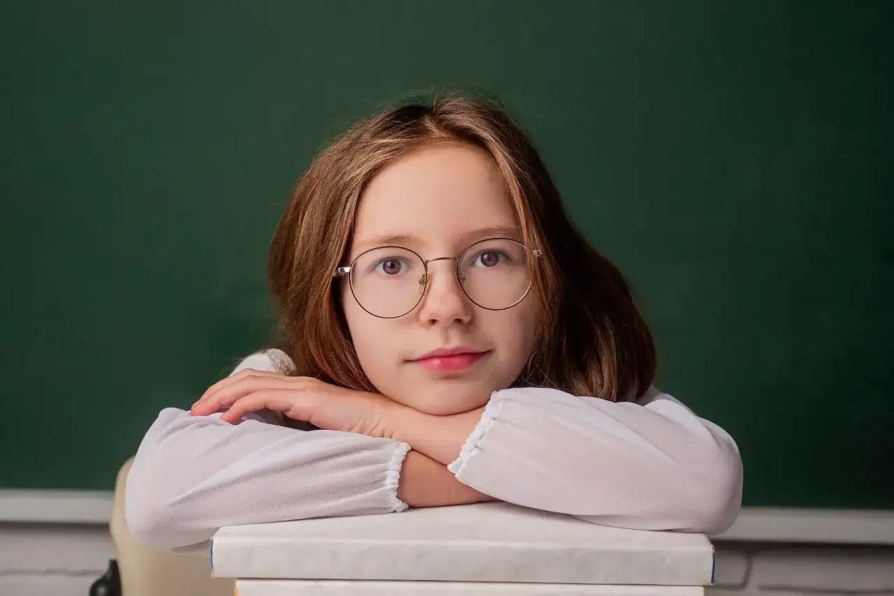 Dziewczynka w okularach opiera się o stos książek. Marzy o nauce i przyszłości, być może o wsparciu 800 plus dla uczących się po 18 roku życia.