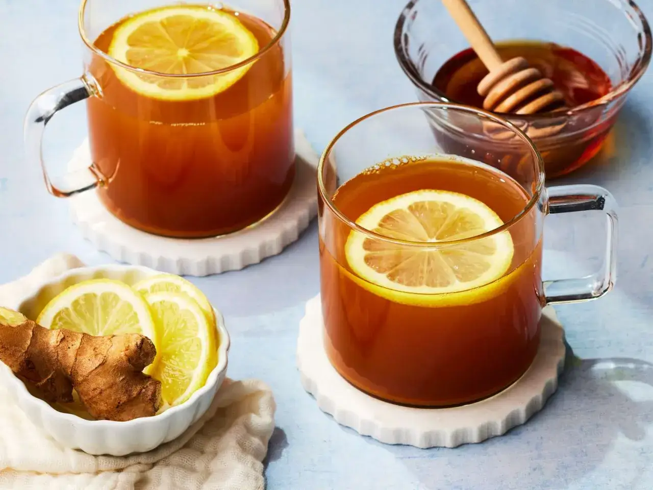 Zwei Tassen warmes Getränk mit Zitrone und Ingwer, perfekt für ein Kurkuma Rezept. Honig und weitere Zutaten sind daneben angerichtet.