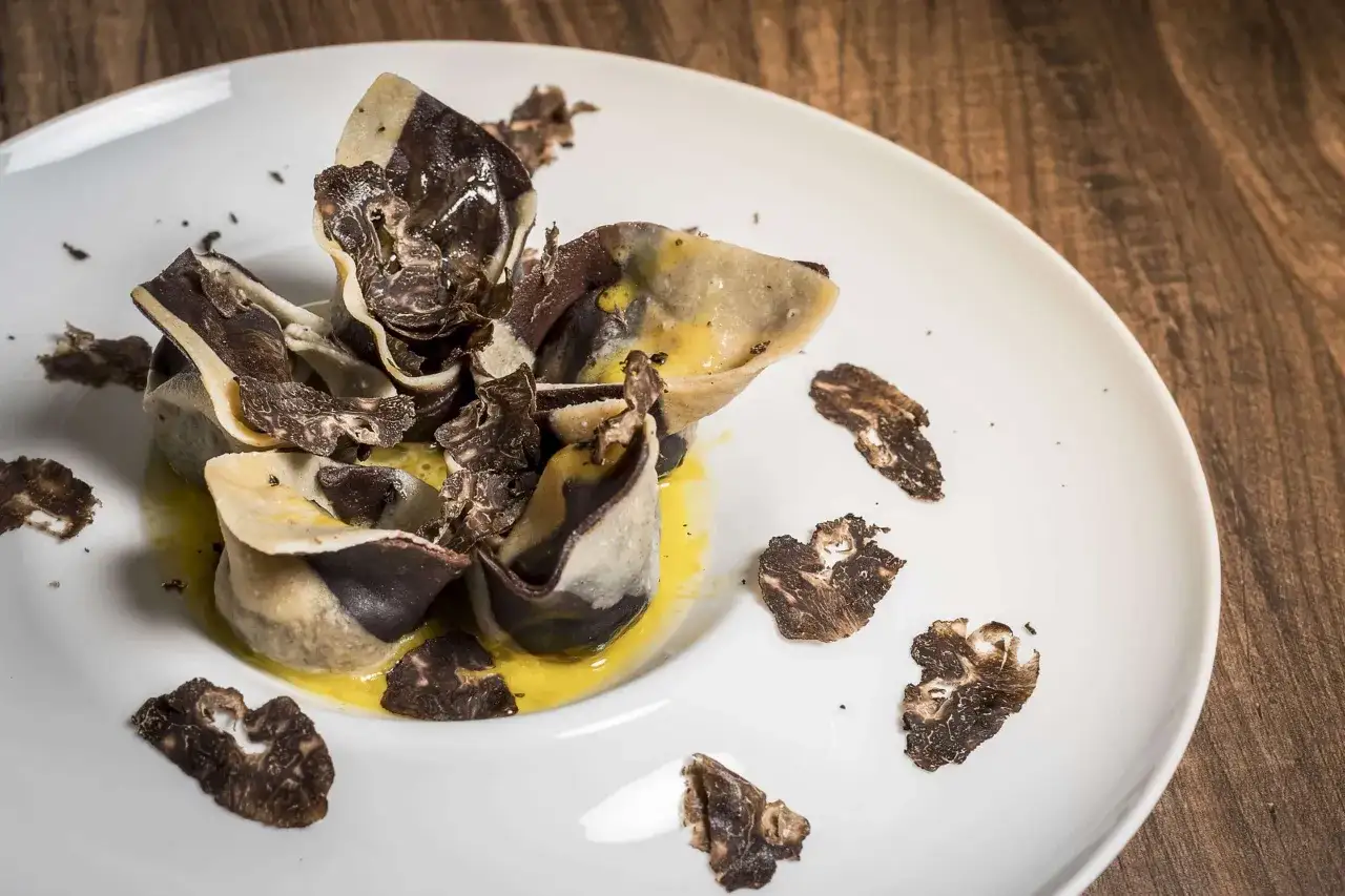 Raviolis bicolores garnis de fines lamelles de diff&eacute;rentes vari&eacute;t&eacute;s de truffes, baignant dans une sauce jaune onctueuse.