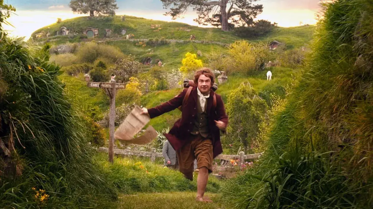 Charakterystyka hobbita: biegnie przez zieloną dolinę Shire, niosąc zwój. W tle widać przytulne nory.