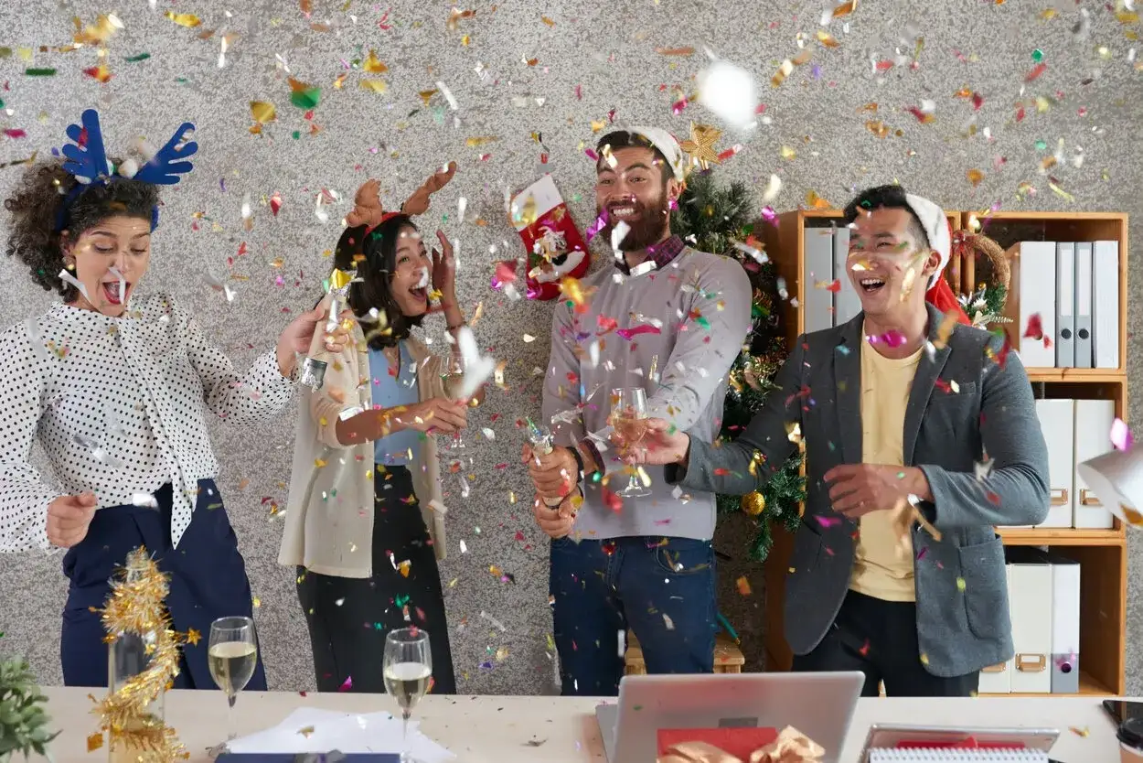 Des coll&egrave;gues c&eacute;l&egrave;brent joyeusement les jeux de no&euml;l entre coll&egrave;gues avec des confettis et des coupes de champagne.